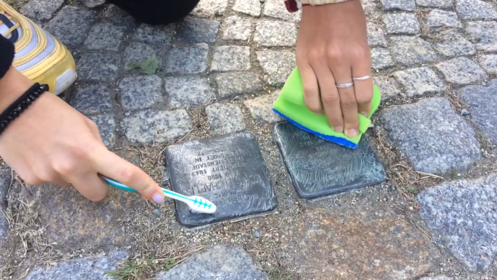 Zu sehen sind zwei Stolpersteine, die mit einer Zahnbürste und einem Schwam gereinigt werden.